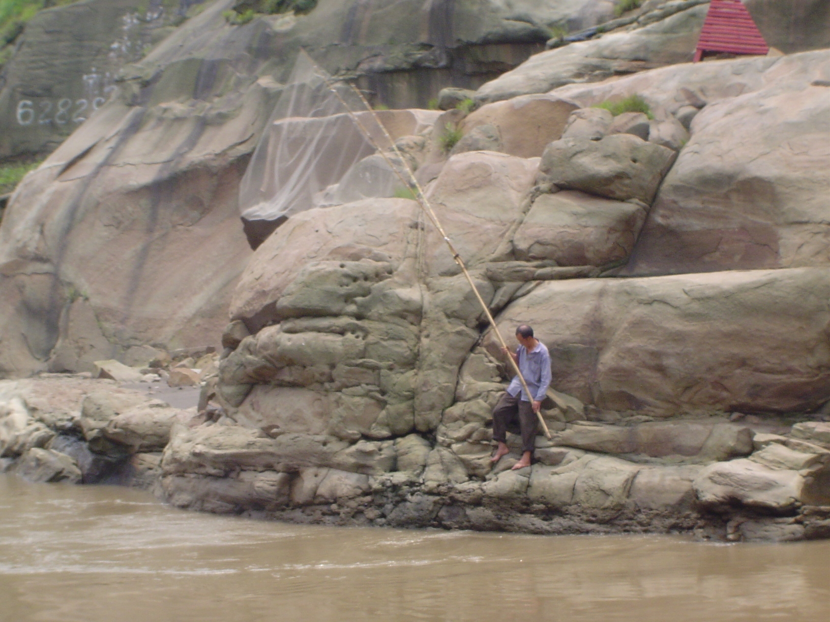 Ignoring all the progress, a fisherman handles his net on the rocky bank. Some 60% percent of all the freshwater fish caught in China—chiefl
