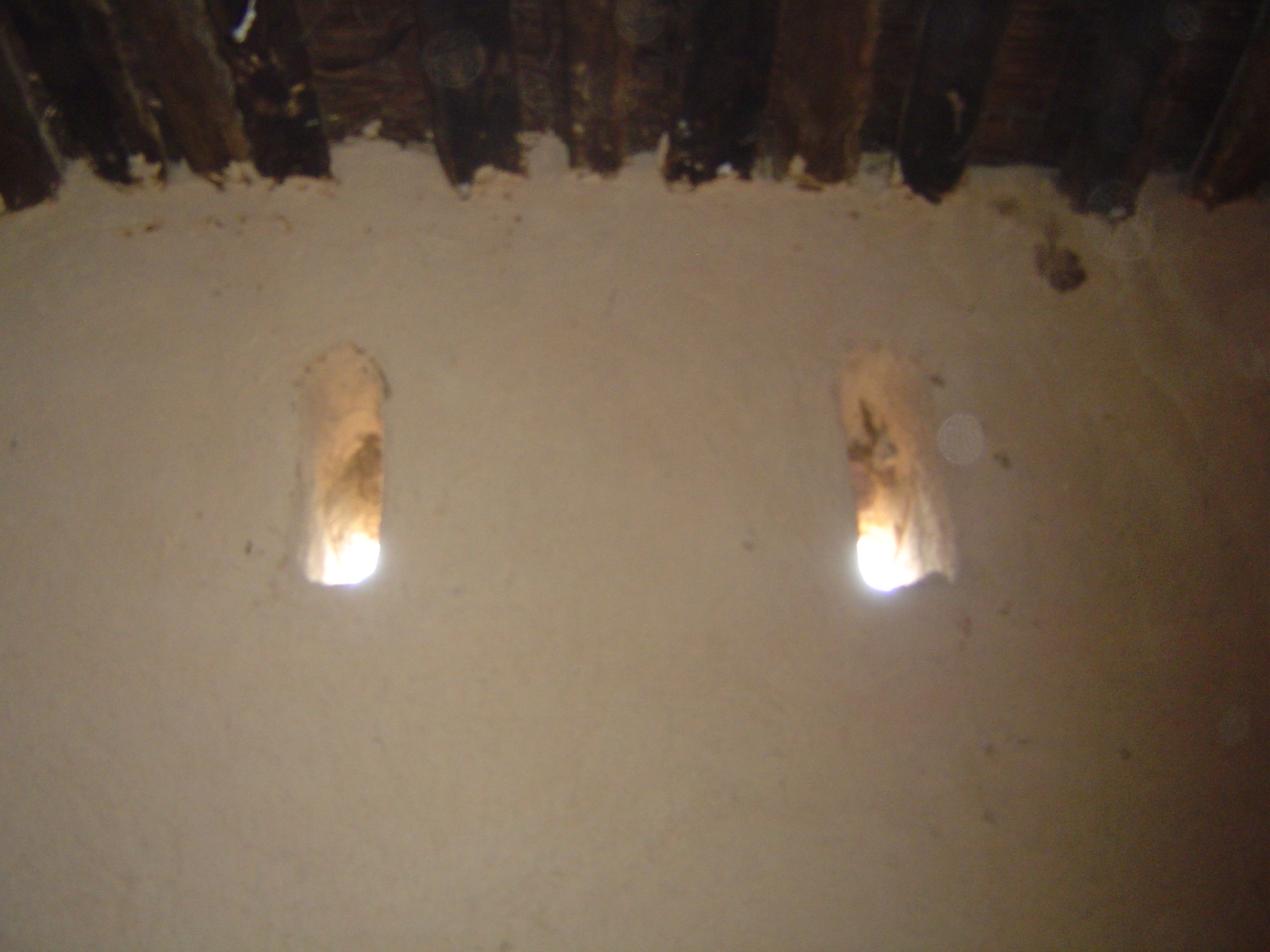 Above, narrow, traditional windows and a palm-log ceiling.