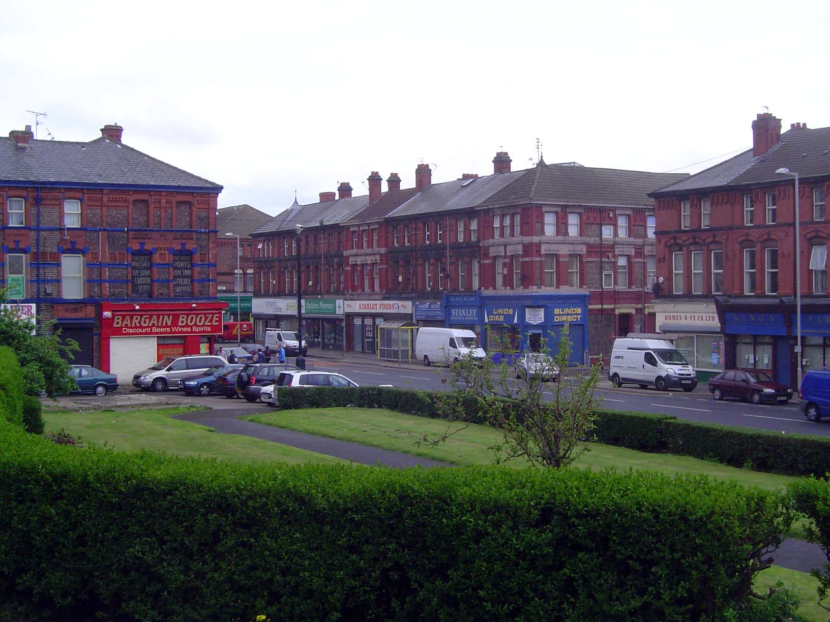 A commercial district in a residential area: Stanley Road in the suburb of Bootle. The camera is near a statue surveying the street.