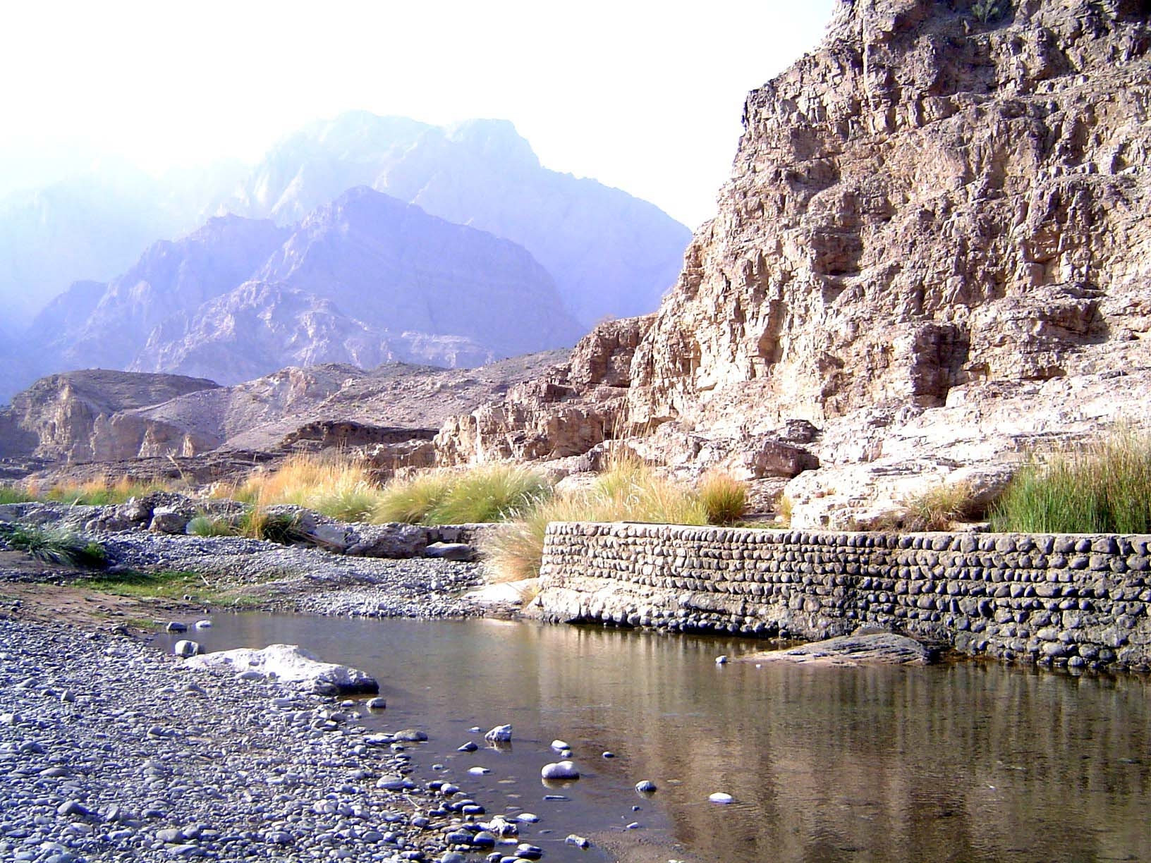 Most of the water is now in the canal behind the stone wall. In the background, the Hajars.