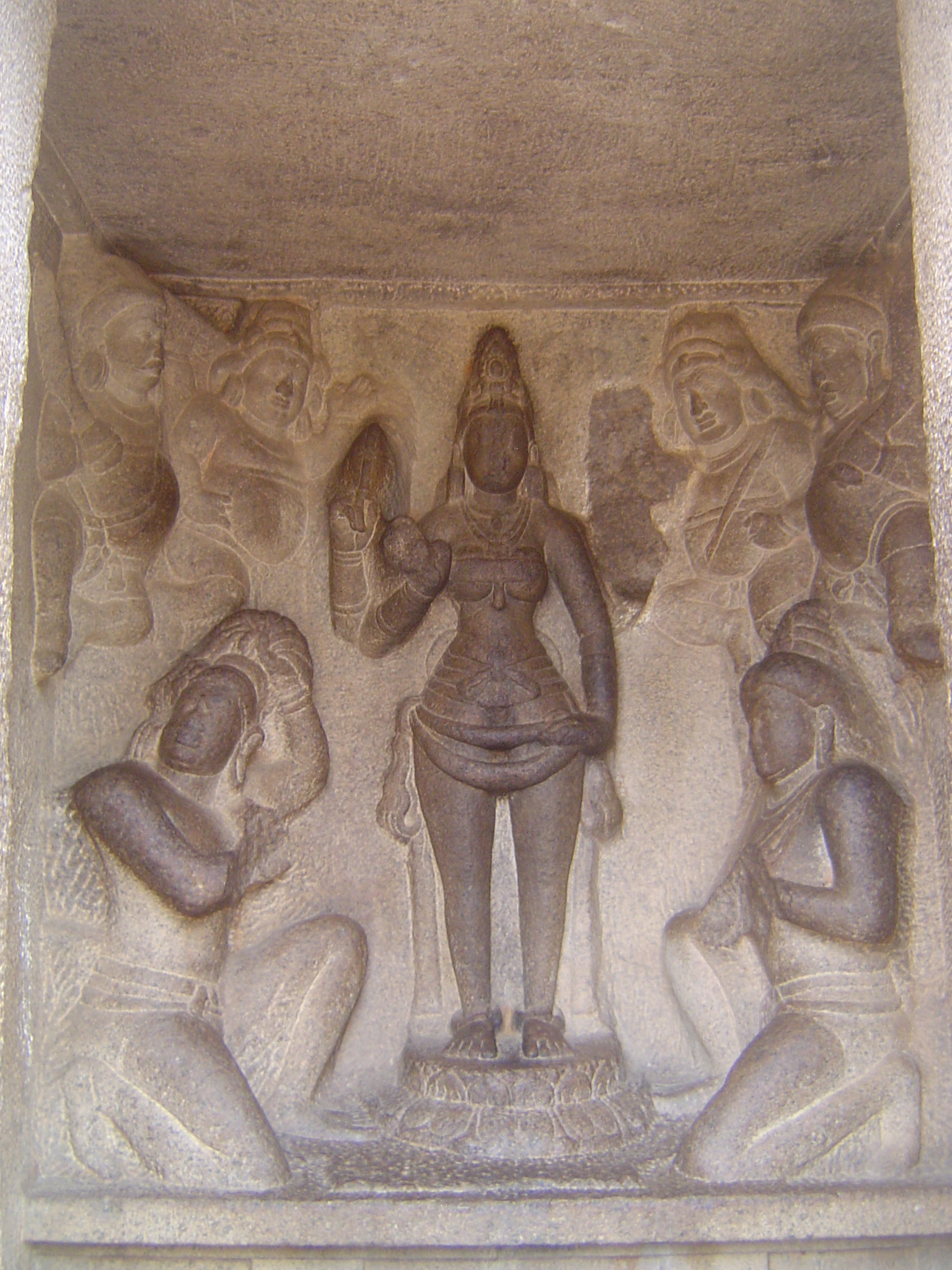 Inside the shrine, Durga and her ganas or attendants stand before two devotees. One prepares to cut off his head, while the other hopes that