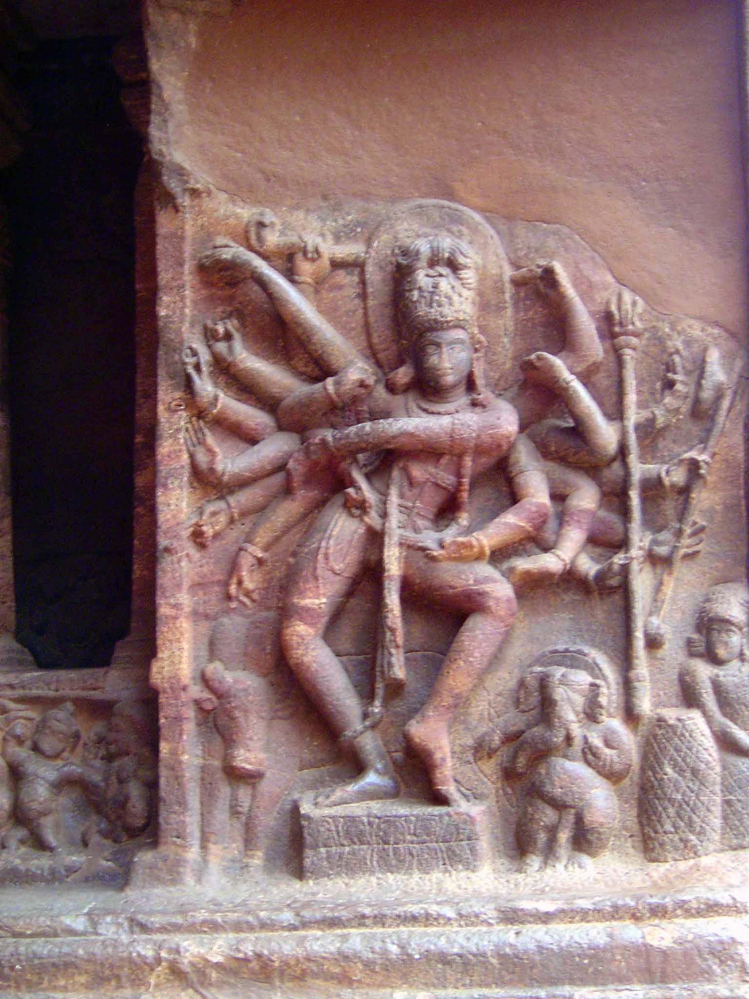 Shiva dances the Tandava, the dance signalling the destruction of the world. He has 18 hands, most with iconic objects including the dmaru,