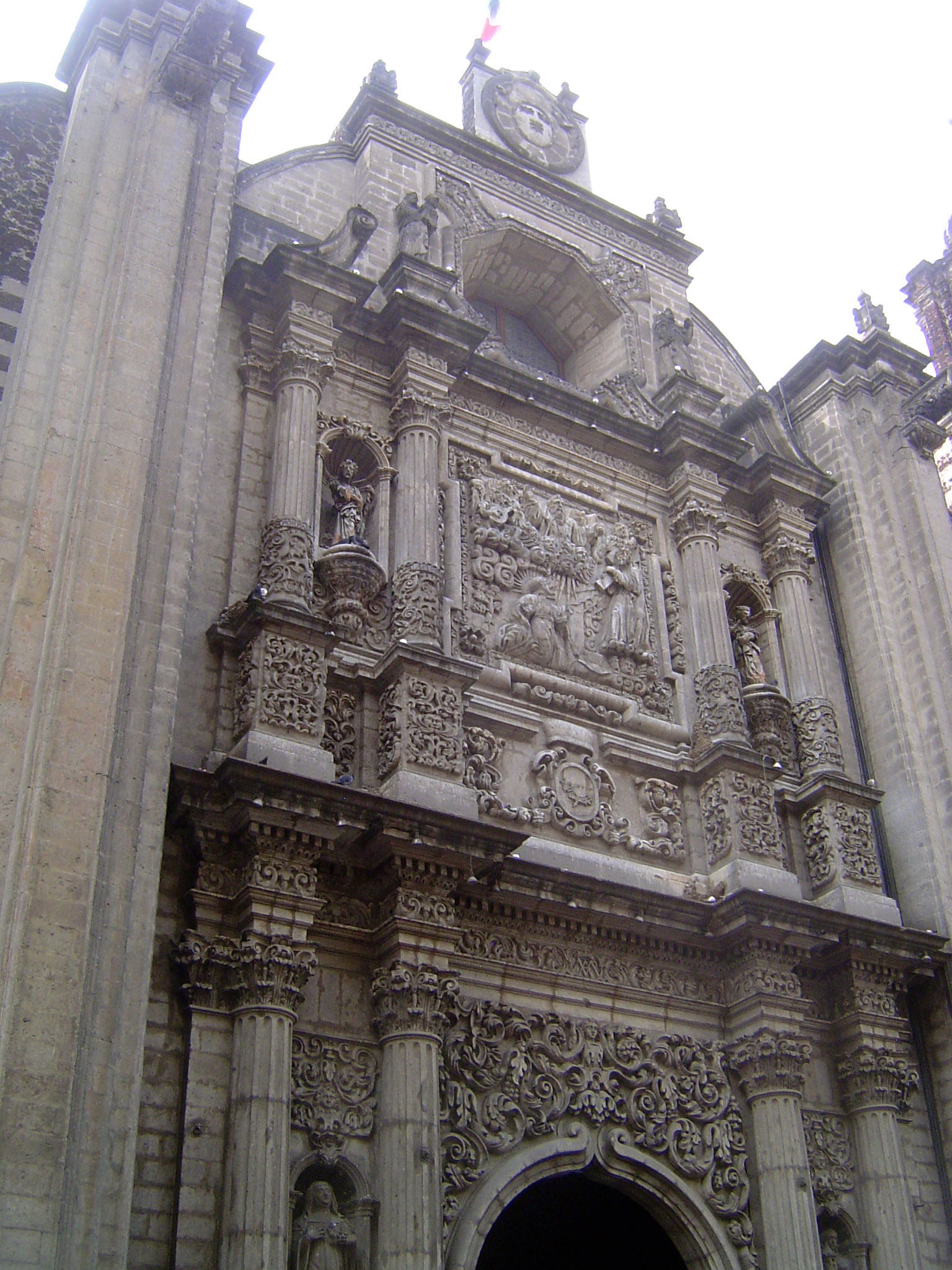 The baroque facade has a central panel showing Christ appearing to St. Ignatius, founder of the Jesuits. The flanking saints squeezed by col
