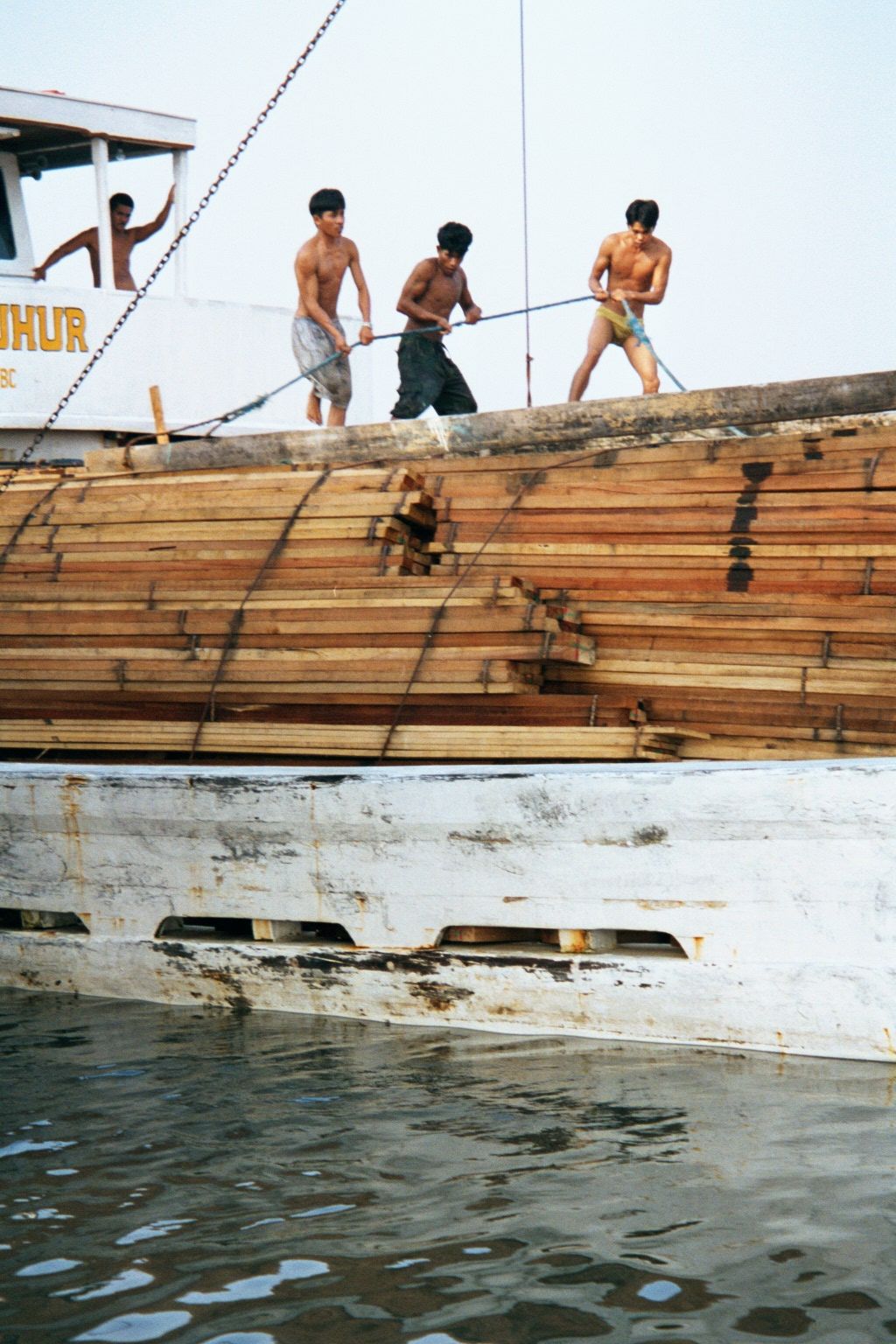 A crew manhandles the gangplank atop lashed timber.